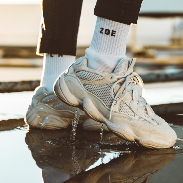 a close up of a person wearing a pair of white sneakers posing over a puddle of water.
